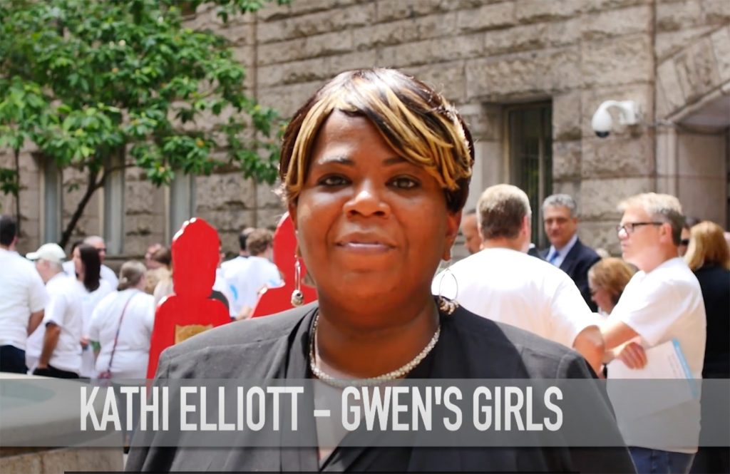 Kathi Elliot, a black woman and founder of gwen's girls, standing outside at an event with people in white t-shirts