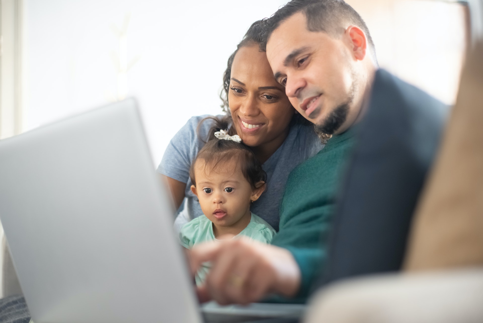A happy interracial couple with a young daughter with down syndrome look and point at a computer screen together.