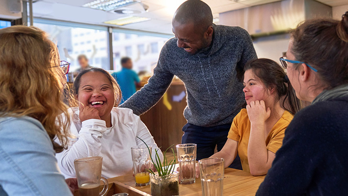 Happy young women with Down Syndrome in cafe with friends