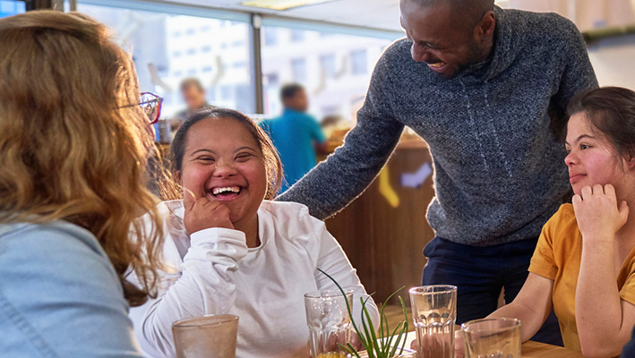 Happy young women with Down Syndrome in cafe with friends
